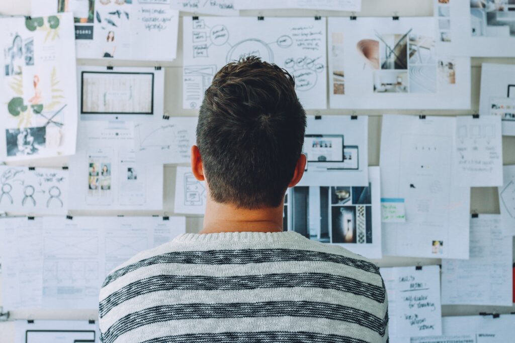 Mann steht vor einer Pinnwand mit vielen Zetteln. Er sucht Orientierung. Mit beruflichem Coaching und Job Coaching den Überblick behalten.